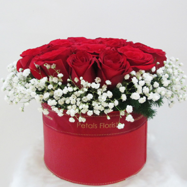 A chic arrangement of red roses and babys’s breath in a round red box.