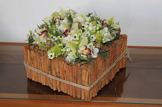 Contenitore realizzato con bastoncini di cannella nel quale trova posta una composizione di orchidee, ornitogallo e alstromeria
